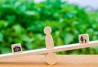 a wooden balance beam with a money symbol being weighed down by a symbol that represents quality of life