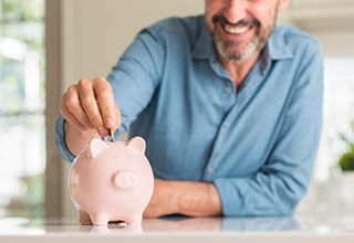 man putting coins into a pink piggy bank 