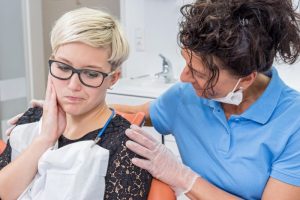 a female patient holding her cheek in pain while a dentist comforts her