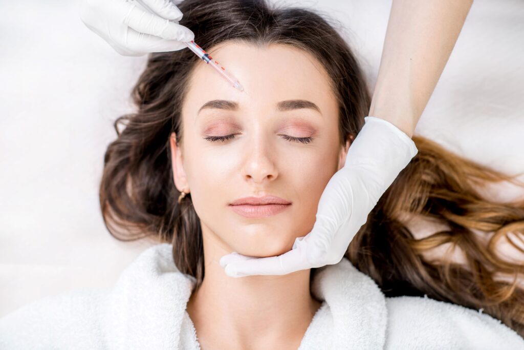 Woman in white robe with eyes closed getting Botox in forehead